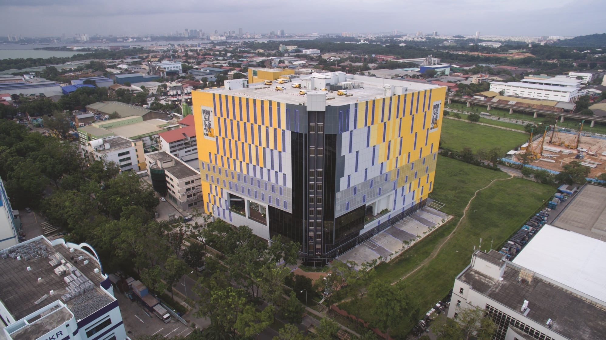 Aerial view of a colorful, cube-shaped building with yellow and blue vertical stripes, surrounded by trees and other buildings.